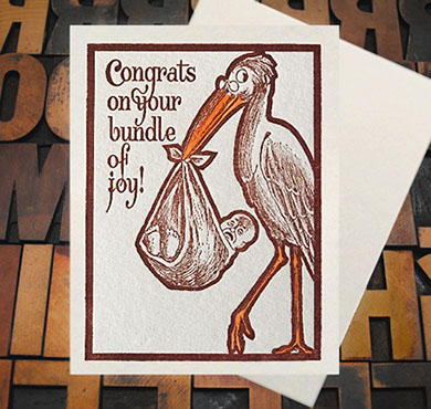 Letterpress Card with an image of a stork carrying an upset baby in a sack with the text, "Congrats on your bundle of joy!"